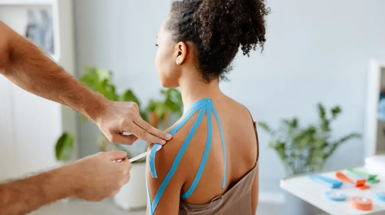 Therapeut legt blaues Kinesio-Tape an Schulter an. Vielleicht ein neues, modernes "Omas Hausmittel gegen Schulterschmerzen"?