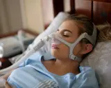 Junge Frau mit Schlafmaske, die gegen Schlafapnoe durch Stress hilft.