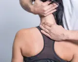 Hände eines Therapeuten untersuchen den Nacken einer Frau, um schmerzen seitlich am Hals entlang zu lindern.