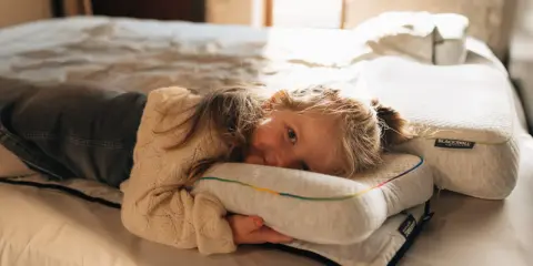 Ein kleines Mädchen kuschelt sich auf einem Bett an ein Kissen. Die Schlafphasen von Kindern sind wichtig für ihre Entwicklung.