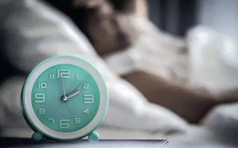 Ein Wecker neben einer schlafenden Person. Die Zeit ist kurz vor 2 Uhr. Ein Symbol für den zirkadianen Rhythmus.