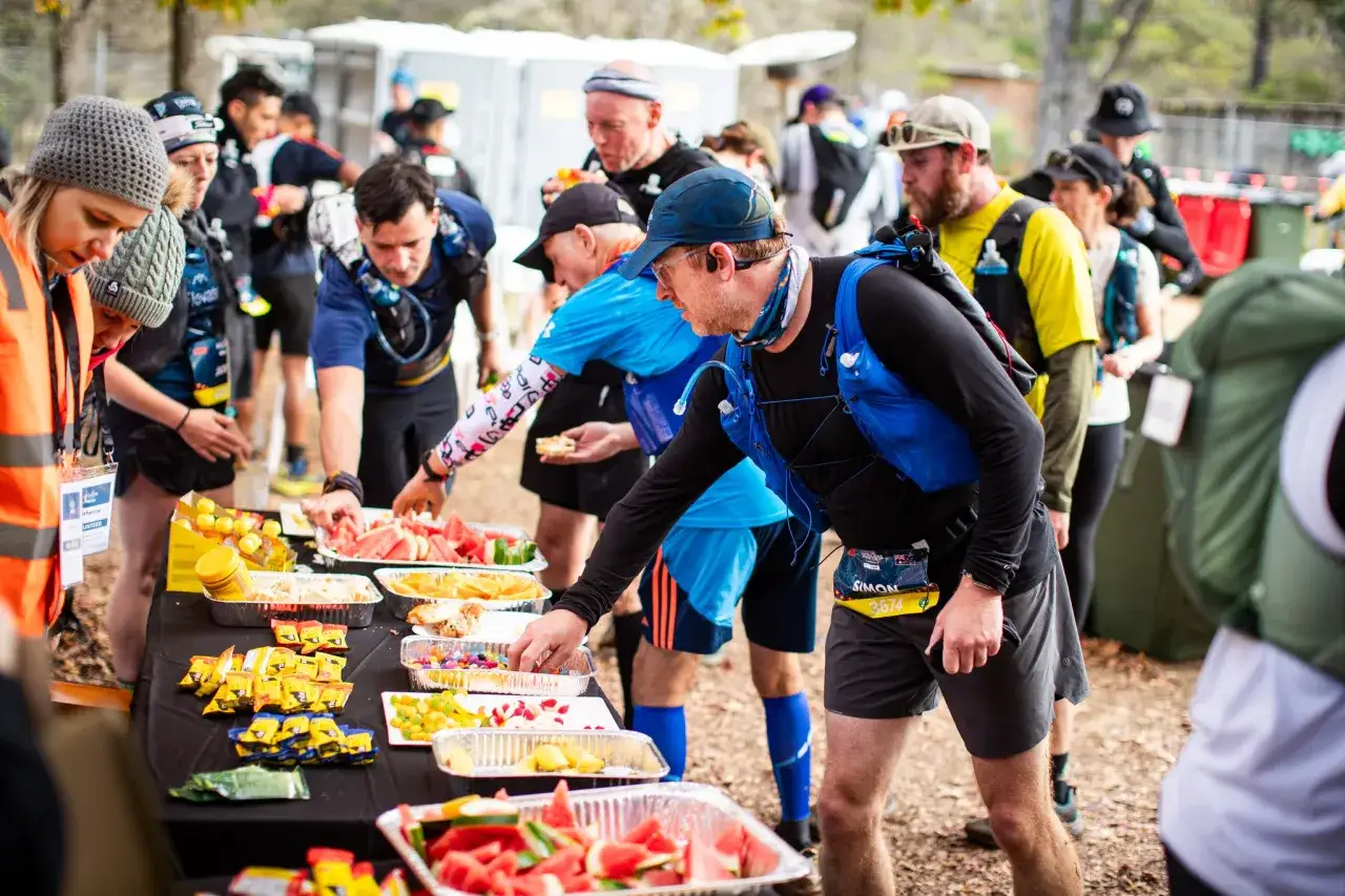 L&auml;ufer bedienen sich an einem Verpflegungsstand. Das ist typisch f&uuml;r einen Ultramarathon, wo Ausdauer und Ern&auml;hrung entscheidend sind.