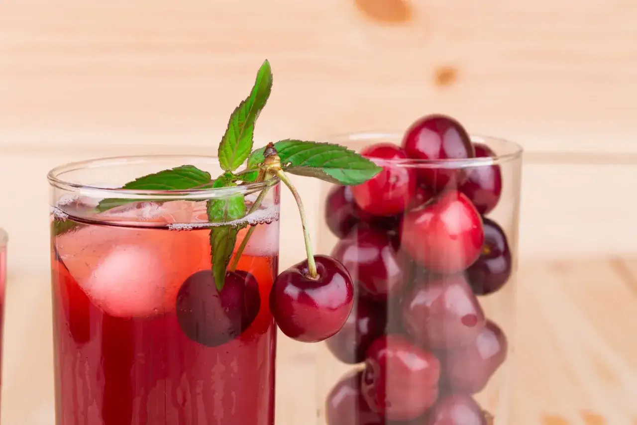 Erfrischender Sauerkirschsaft mit Eis und Minze, daneben ein Glas voller Kirschen. Die Wirkung von Sauerkirschsaft ist bekannt f&uuml;r seine entz&uuml;ndungshemmenden Eigenschaften.