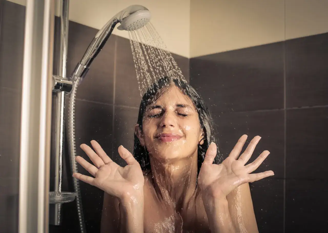 Frau unter einer kalten Dusche, Wasser läuft über ihr Gesicht und ihre Hände.