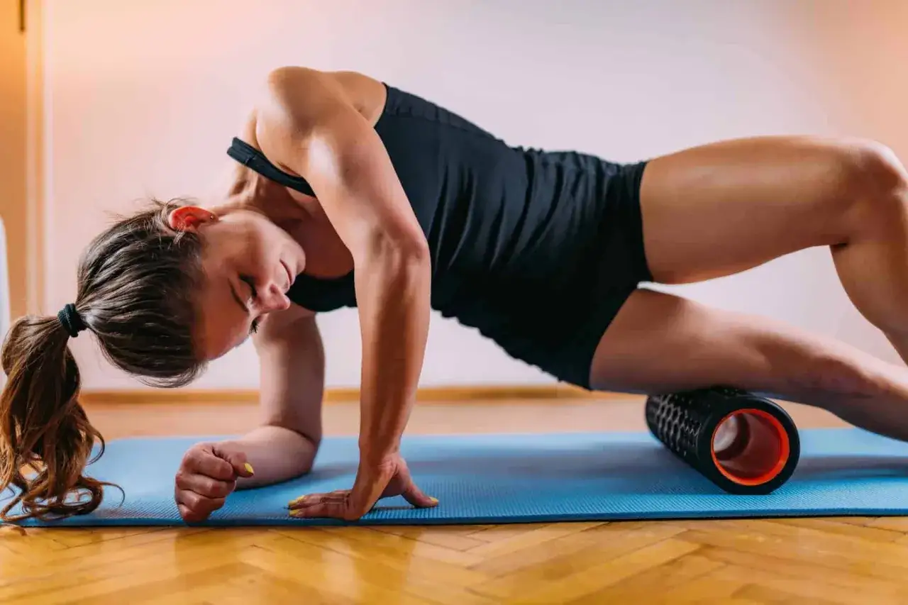 Frau macht Foam Rolling auf einer blauen Matte, um ihre Muskeln zu lockern.