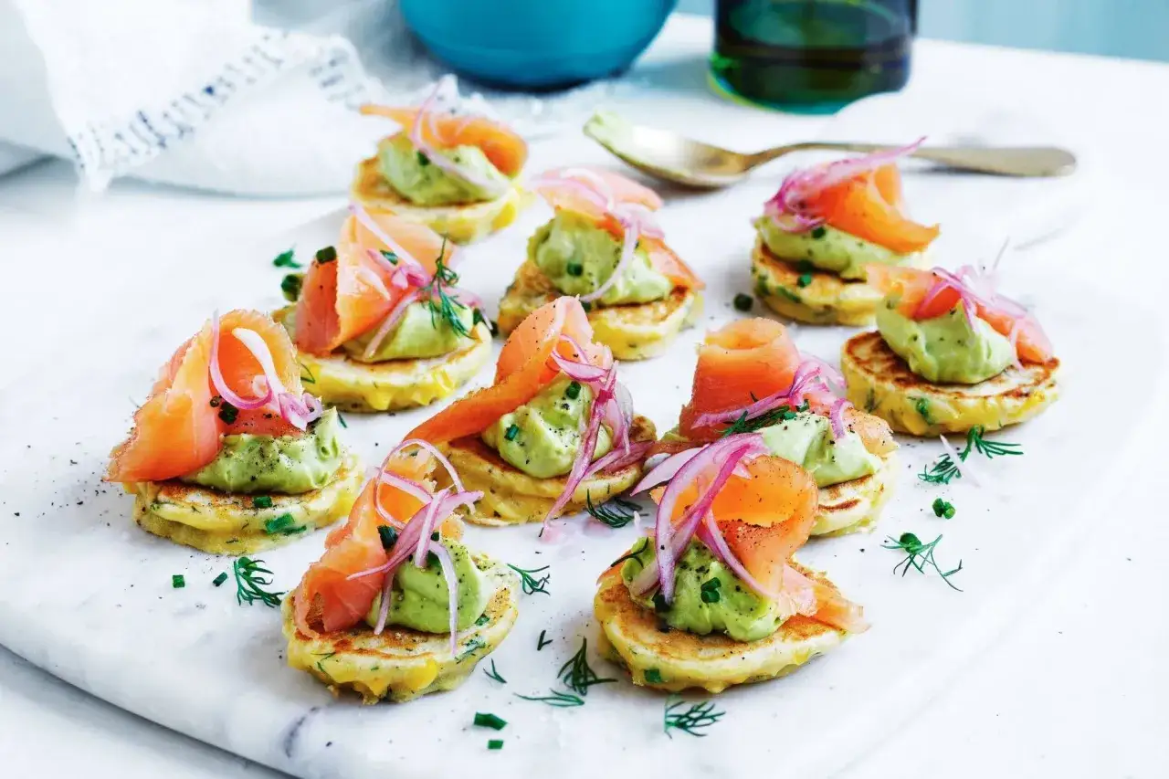 Kleine Pfannkuchen mit Avocado-Creme, Räucherlachs und roten Zwiebeln – ein köstliches und gesundes Fingerfood.