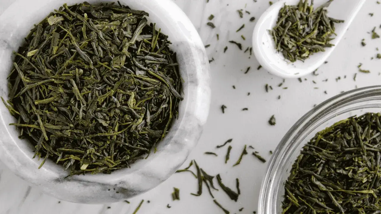 Trockene Sencha-Teebl&auml;tter in einer Marmorschale und einem L&ouml;ffel. Die Sencha Tee Wirkung ist belebend und erfrischend.