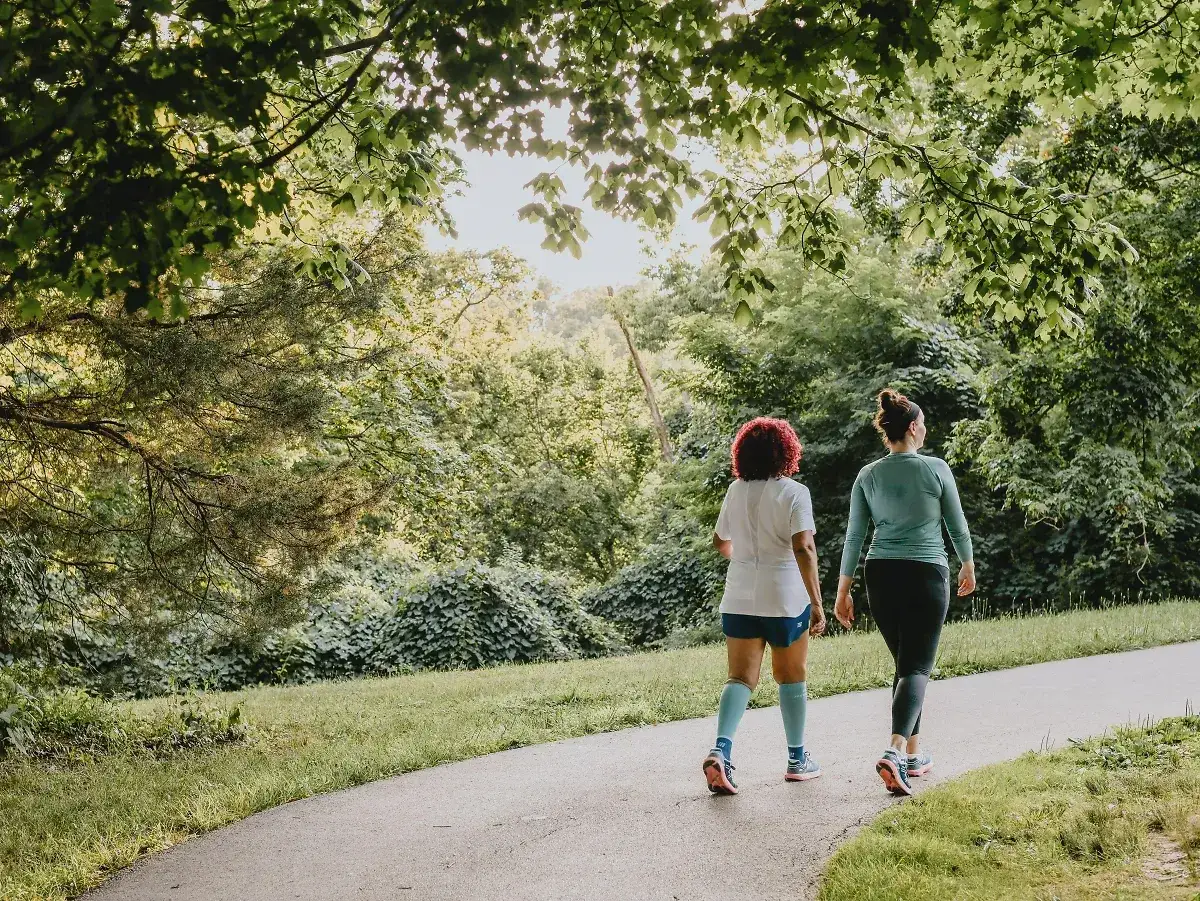 Zwei Frauen joggen auf einem Weg im Gr&uuml;nen. Sie genie&szlig;en die frische Luft und die Natur. Was bringt joggen? Gesundheit und Wohlbefinden!