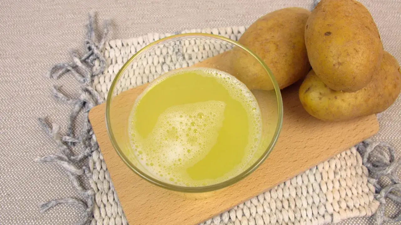 Frischer Kartoffelsaft in einer Schale, daneben rohe Kartoffeln. Ein Hausmittel gegen Sodbrennen.