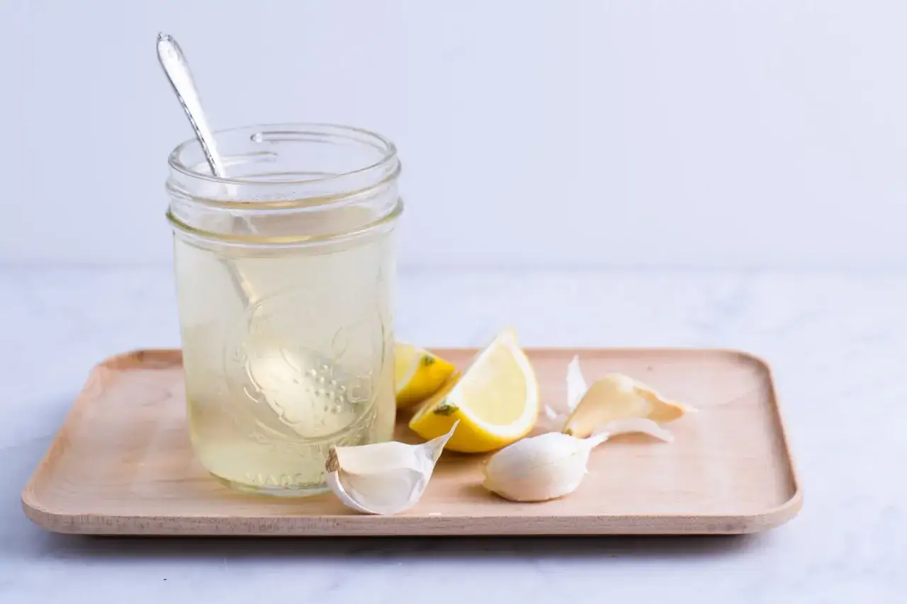 Glas mit Fl&uuml;ssigkeit, Zitronenspalten und Knoblauchzehen. Ein einfaches Rezept f&uuml;r eine Knoblauch-Zitrone-Kur.